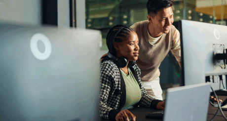 A woman and man look at a computer monitor in an office setting.