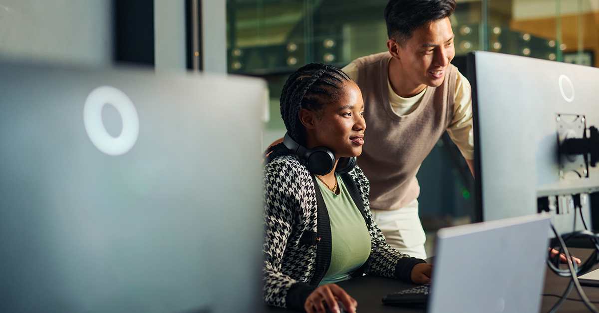 A woman and man look at a computer monitor in an office setting.